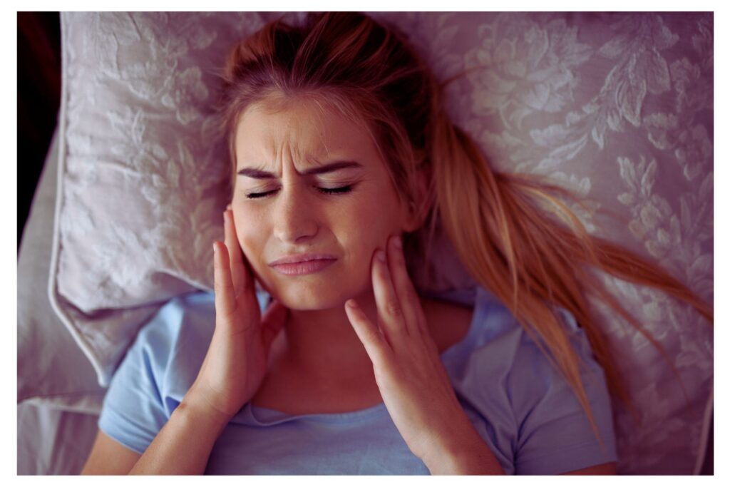 Photo of a woman waking up and holding her jaw due to pain from clenching her teeth while sleeping.