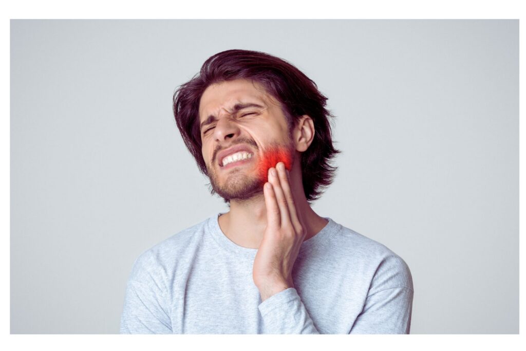 Photo of a man touching his cheek in pain from biting down.